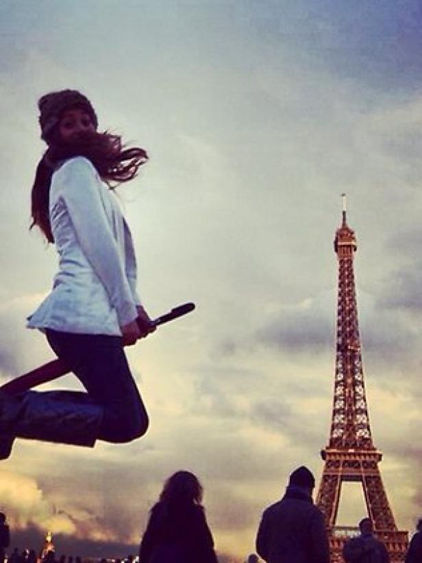 Eine Frau „fliegt“ auf einem Besen vor dem Eiffelturm in Paris.