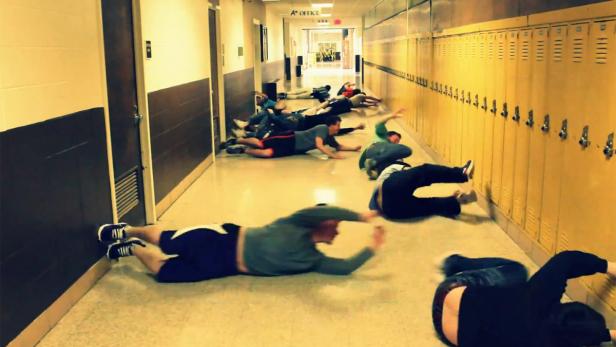 Eine Gruppe von Menschen liegt bäuchlings in einem Flur mit Schließfächern.