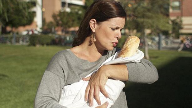 Eine Frau wiegt ein Baguette, das in ein weißes Tuch gewickelt ist, wie ein Baby.
