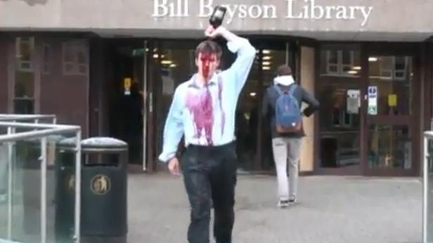 Ein Mann steht vor der Bill Bryson Library und übergießt sich mit einer Flüssigkeit.