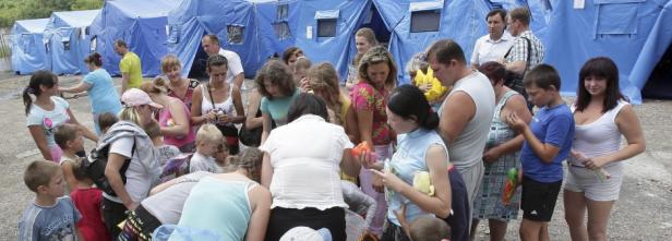 Vor blauen Zelten stehen Menschen, darunter viele Kinder.