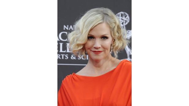 Jennie Garth trägt ein orangefarbenes Kleid und lockiges blondes Haar.