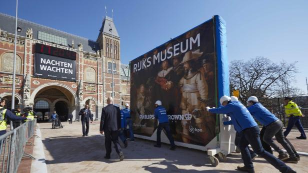 Arbeiter transportieren eine große Reproduktion von Rembrandts „Die Nachtwache“ vor dem Rijksmuseum.