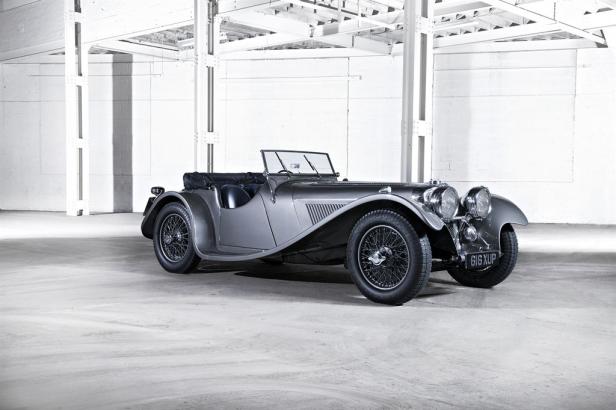 Ein grauer Oldtimer-Sportwagen steht in einer Lagerhalle.