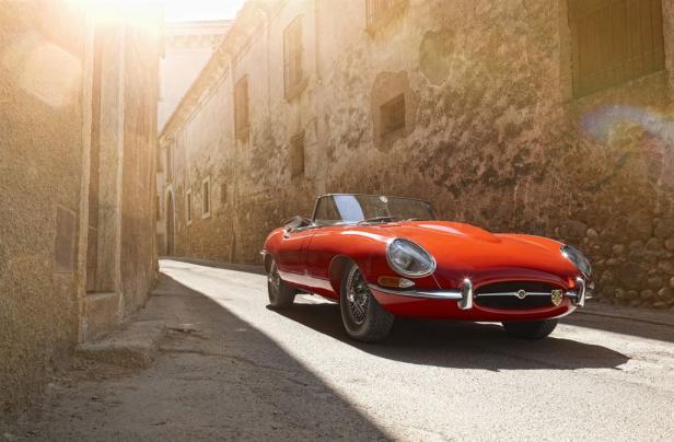Ein roter Jaguar E-Type Roadster fährt durch eine enge Gasse.