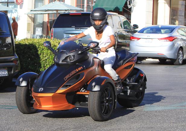 Eine Frau mit Helm fährt ein orangefarbenes Can-Am Spyder Dreirad.