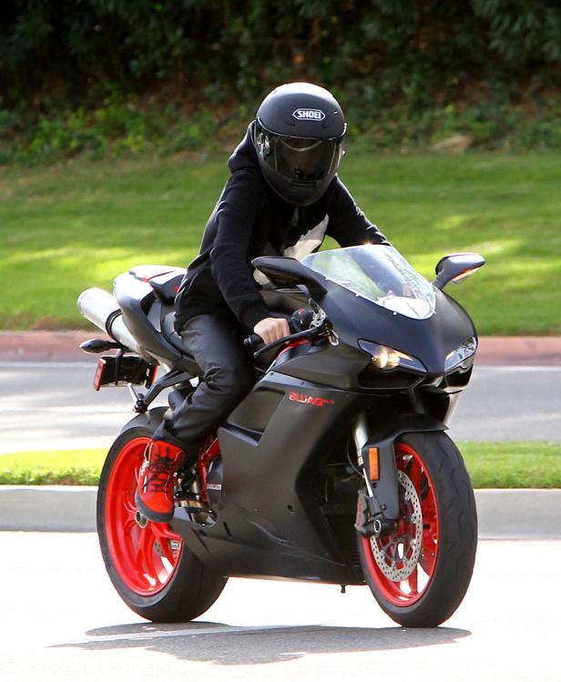 Eine Person mit Helm fährt auf einer schwarzen Ducati mit roten Felgen.