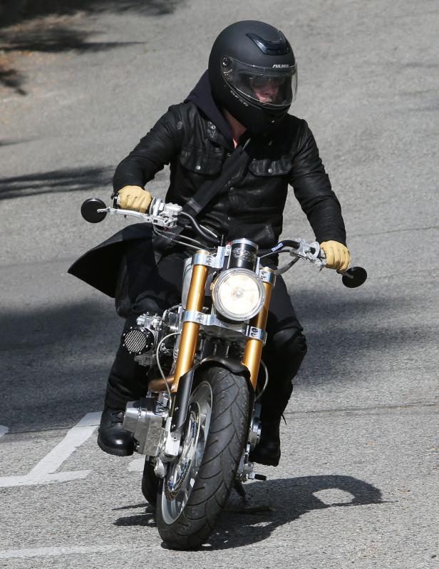 Eine Person mit Helm fährt ein Motorrad auf einer asphaltierten Straße.