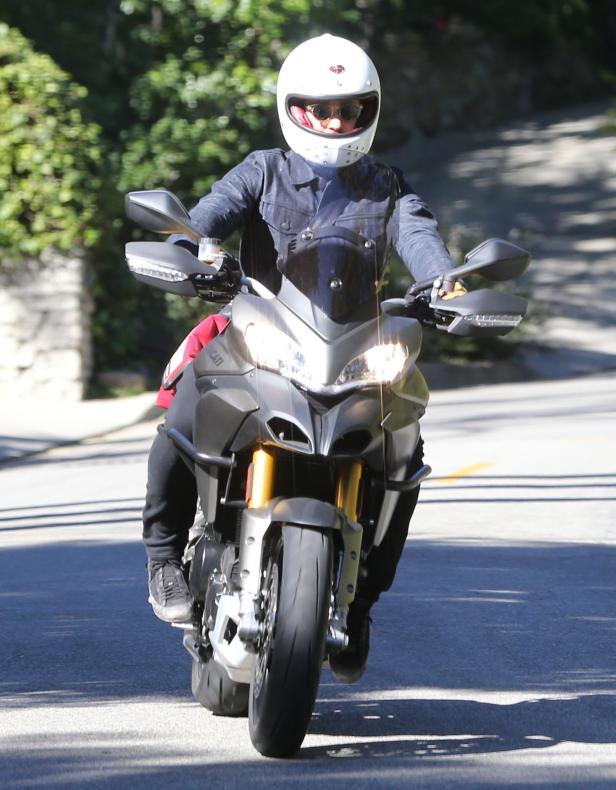 Eine Person mit Helm fährt ein Ducati-Motorrad auf einer Straße.