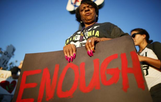 Eine Frau hält ein Schild mit der Aufschrift „Enough“ in roter Farbe.