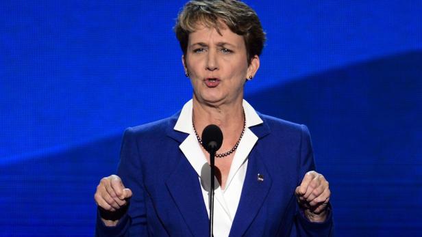 Eine Frau in einem blauen Blazer spricht vor einem blauen Hintergrund.