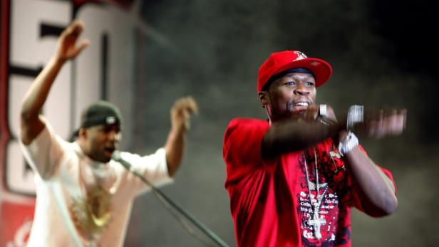 50 Cent rappt mit erhobenen Händen auf einer Bühne.