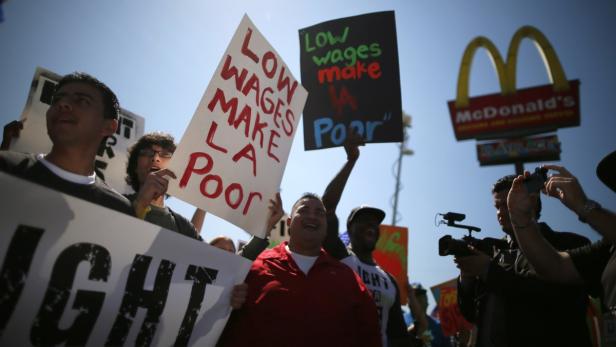 Menschen demonstrieren vor einem McDonald's-Restaurant mit Schildern, die niedrigere Löhne anprangern.