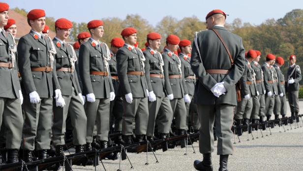 Eine Reihe Soldaten in Uniformen und roten Baretts steht Gewehr bei Fuß.