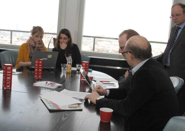 Mehrere Personen sitzen an einem Tisch und arbeiten an Laptops und Dokumenten.