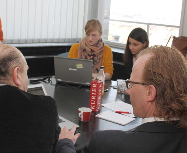 Mehrere Personen sitzen an einem Tisch mit Laptops und Getränken.