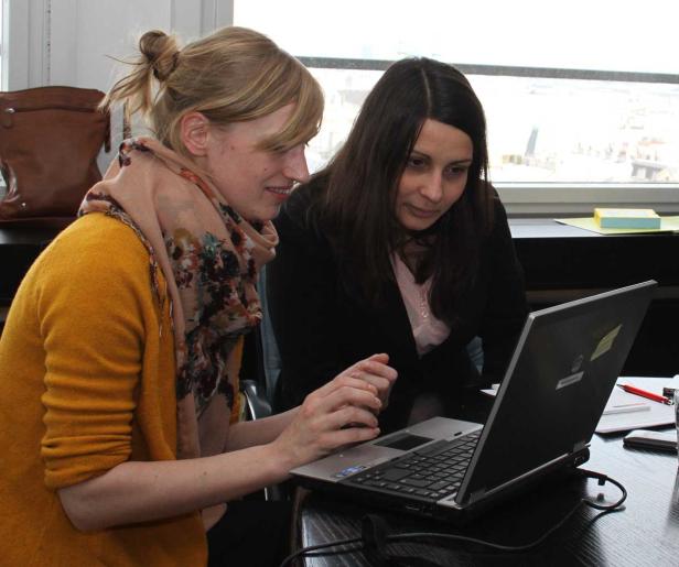 Zwei Frauen sitzen an einem Tisch und arbeiten gemeinsam an einem Laptop.