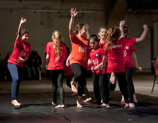 Eine Gruppe barfüßiger Mädchen in roten T-Shirts tanzt auf einer Bühne.
