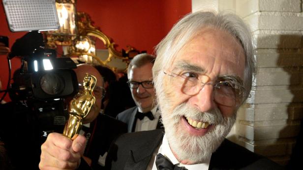 Ein Mann mit Brille und Bart hält eine goldene Oscar-Statue in die Höhe.