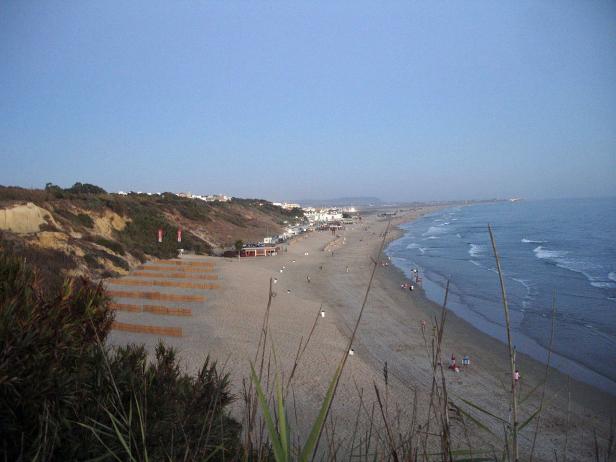 Blick von einer Düne auf einen Sandstrand mit Badegästen.