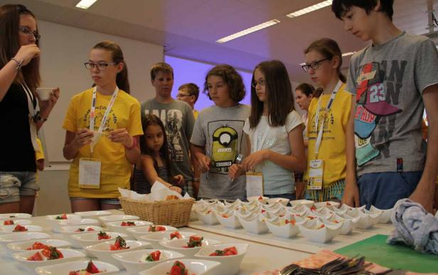Eine Gruppe von Kindern steht an einem Tisch mit kleinen Schüsseln mit Erdbeeren und Joghurt.
