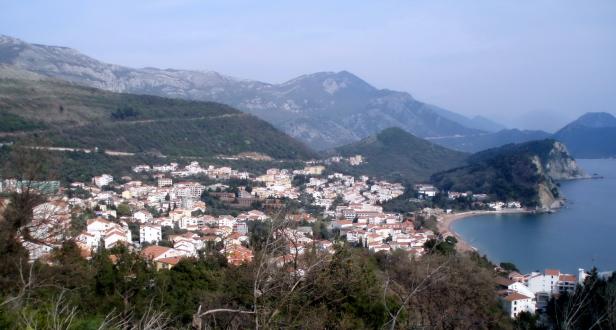 Blick auf eine Küstenstadt mit roten Dächern und Bergen im Hintergrund.