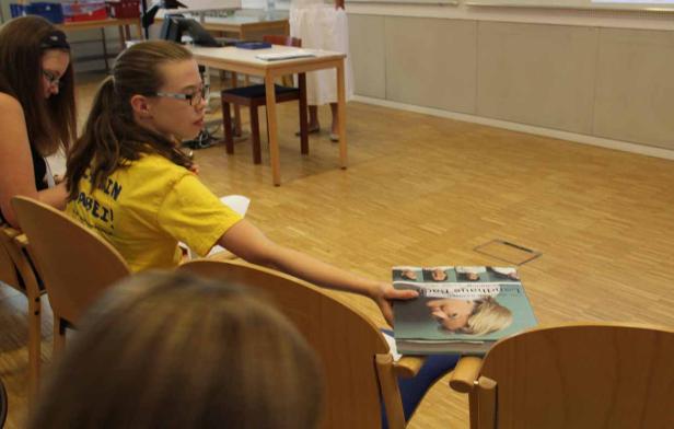 Ein Mädchen mit Brille reicht ein Buch mit dem Titel „Landhaus Hack“ weiter.
