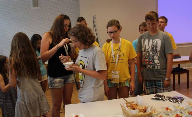 Eine Gruppe Jugendlicher steht an einem Tisch und isst aus kleinen Schüsseln.