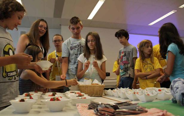 Eine Gruppe von Kindern steht an einem Tisch mit kleinen Schüsseln mit Speisen.