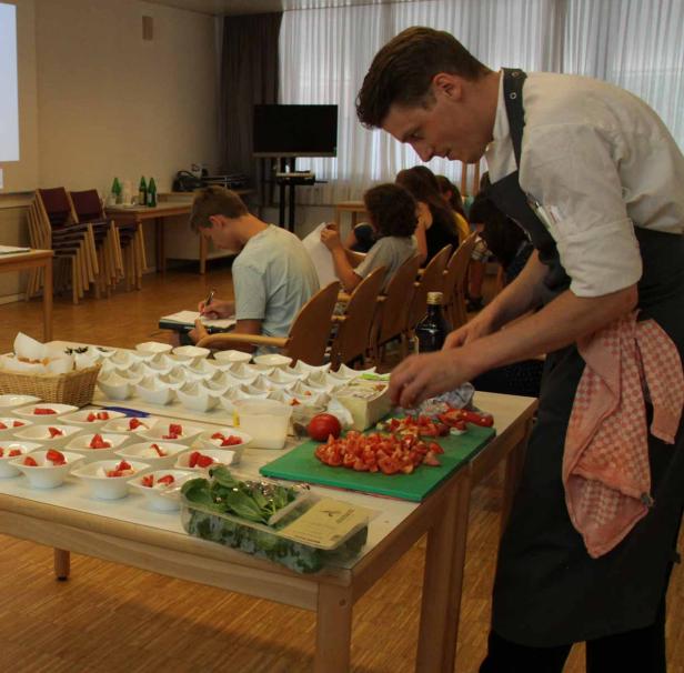 Ein Koch bereitet Tomaten und Mozzarella für eine Gruppe von Personen zu.