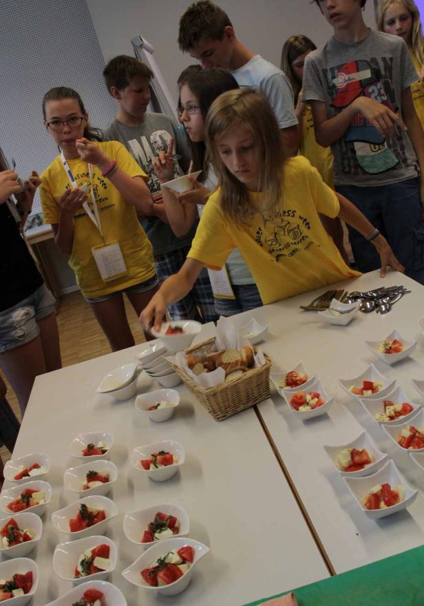 Eine Gruppe Jugendlicher bedient sich an einem Tisch mit Tomaten-Mozzarella-Salat und Brot.
