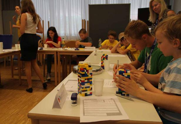 Kinder bauen mit Legosteinen an Tischen in einem hellen Raum.