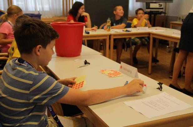 Ein Junge sitzt an einem Tisch und beklebt ein Blatt Papier mit roten Aufklebern.