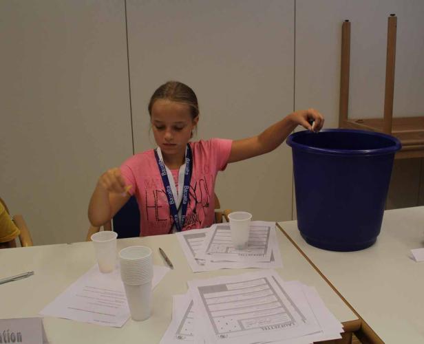 Ein Mädchen wirft einen Zettel in einen blauen Eimer.