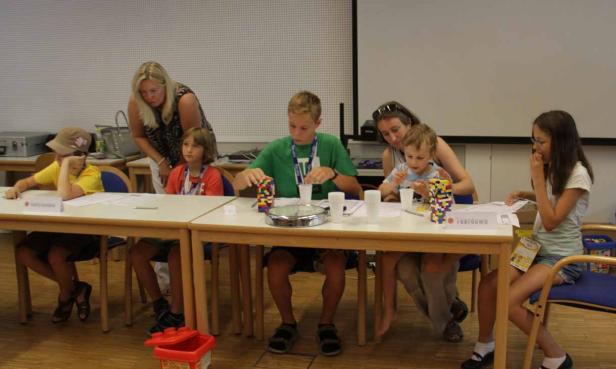 Kinder sitzen an einem Tisch und spielen mit bunten Bauklötzen, während Erwachsene zusehen.