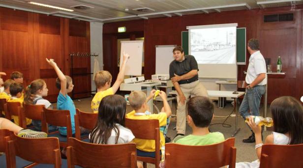 Ein Lehrer hält einen Vortrag vor einer Gruppe von Kindern in einem Klassenzimmer.