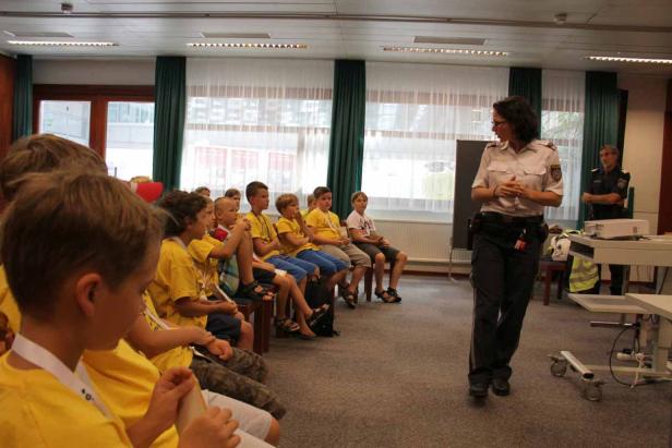 Eine Polizistin spricht vor einer Gruppe von Kindern in gelben T-Shirts.