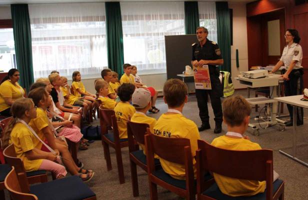Ein Polizist hält einen Vortrag vor einer Gruppe von Kindern in gelben T-Shirts.