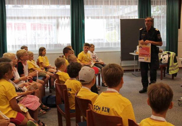Ein Polizist hält einen Vortrag vor einer Gruppe von Kindern in gelben T-Shirts.