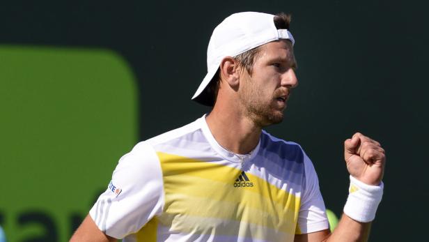 Ein Tennisspieler mit weißer Kappe und gelb-weißem Shirt ballt die Faust.