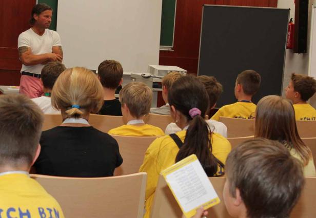 Ein Mann hält einen Vortrag vor einer Gruppe von Kindern in gelben T-Shirts.