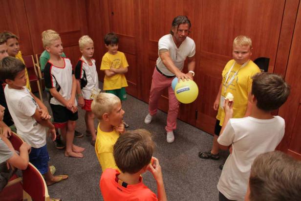 Eine Gruppe Kinder steht um einen Mann, der einen gelben und blauen Ballon hält.