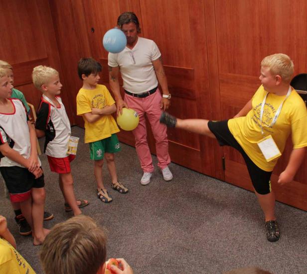 Ein Junge tritt einen Ballon, während andere Kinder und ein Mann zusehen.