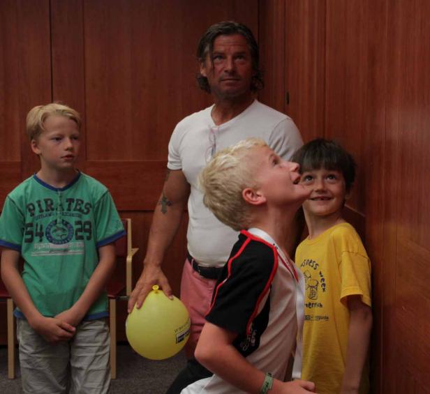 Ein Mann steht mit drei Jungen in einem Raum, einer der Jungen hält einen gelben Ballon.