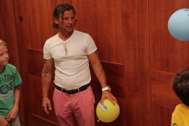 Ein Mann mit Tätowierungen hält einen gelben Ballon in der Hand.