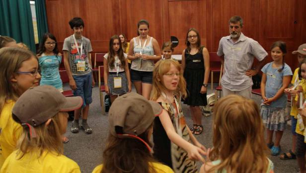 Eine Gruppe von Kindern und ein Mann stehen in einem Kreis in einem Raum.