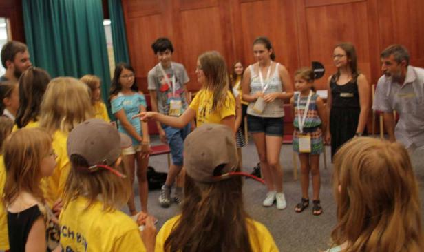 Eine Gruppe von Kindern und Erwachsenen steht in einem Raum und interagiert miteinander.