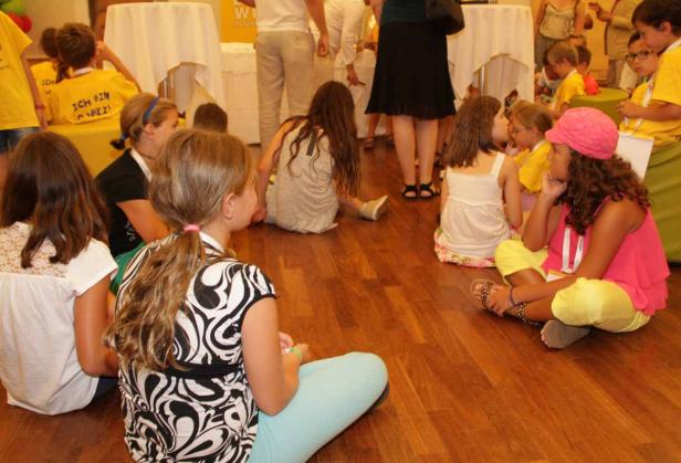 Eine Gruppe von Kindern sitzt auf dem Holzboden.