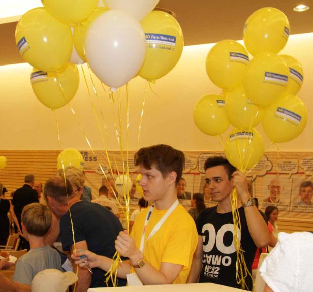 Zwei junge Männer halten gelbe und weiße Luftballons mit der Aufschrift „NÖ Familienland“.