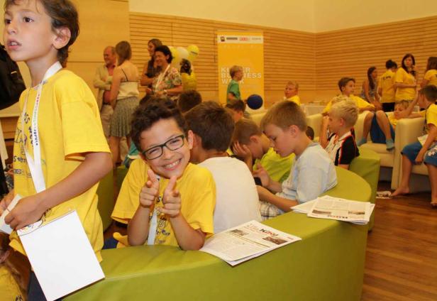Eine Gruppe Kinder sitzt in einem Raum, ein Junge mit Brille lächelt in die Kamera.